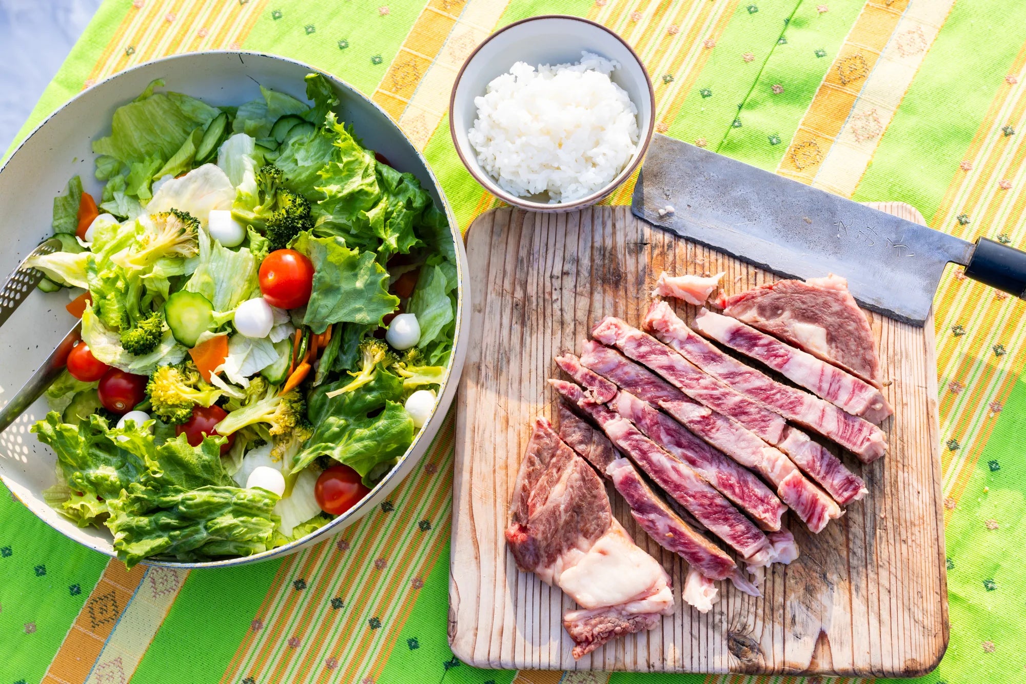 A grilled Wagyu ribeye resting on a wooden cutting board next to a fresh salad and chef's knife