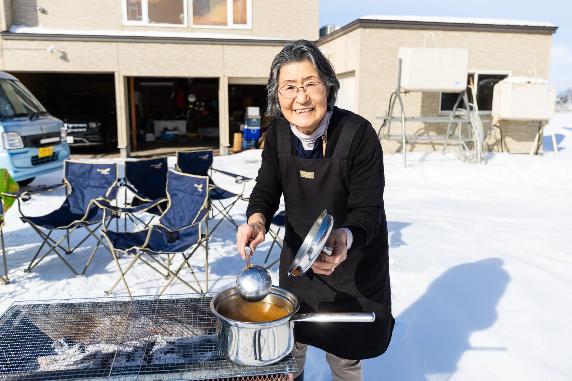 Tomoko-san ladling soup over a charcoal grill in the snow